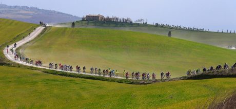 Peloton on a long gravel road with Tuscan landscape.
