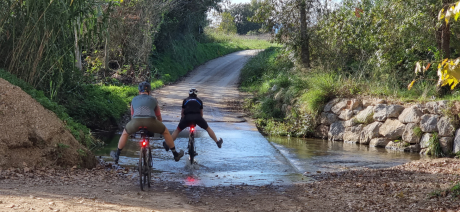 Two gravel riders crossing a stream by bike.