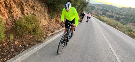 Three cyclists climbing a hill with olive trees in the background