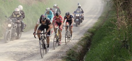 Group of cyclists racing on gravel alongside race officials on motorcycles