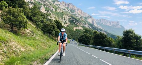 A woman cycling alone on a two-lane road with limestone mountains behind
