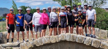 A group of cyclists posing in a line on a Roman bridge